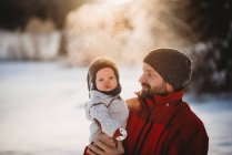 Papai e bebê bonito lá fora na neve no inverno durante o pôr do sol dourado — Fotografia de Stock