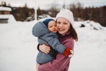 Smiley Big sister segurando irmão bebê fora na neve no frio da — Fotografia de Stock