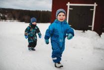Молоді хлопчики-близнюки посміхаються, гуляючи снігом на скандинавській фермі біля сараю. — стокове фото