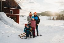 Щаслива усміхнена сім'я на сніговій сільській фермі під час заходу сонця — стокове фото