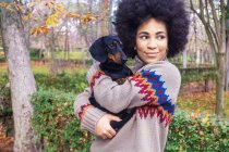 Afroamerikanerin sitzt im Herbst im Park und umarmt ihren Hund — Stockfoto
