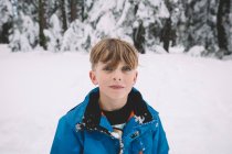 Rubio chico con ojos azules de pie en un campo cubierto de nieve - foto de stock