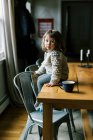 Маленькая девочка сидит на столе в уютном домашнем шерстяном свитере — стоковое фото