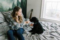 Mujer con su perro caniche negro en la cama alimentándolo trata - foto de stock