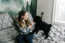 Frau mit schwarzem Pudelhund auf dem Bett füttert ihn mit Leckereien — Stockfoto