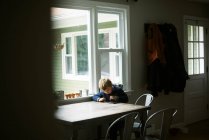 Piccolo ragazzo indipendente che usa il suo tablet per la scuola remota a un tavolo — Foto stock