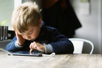 Menino independente usando seu tablet para escola remota em uma mesa — Fotografia de Stock