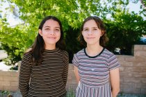 Hermanas con rayas de contraste ofrecen sonrisas educadas a la cámara - foto de stock