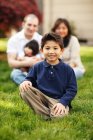 Garçon assis et souriant devant la famille dans l'herbe — Photo de stock