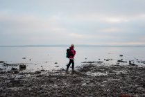 Mujer con una mochila caminando por la costa inglesa sola - foto de stock