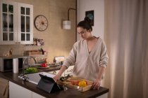 Молода жінка переглядає рецепт на планшеті під час приготування салату на кухні вдома — стокове фото