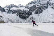 Hombre jugando hockey cerca de las montañas nevadas en el lago congelado - foto de stock