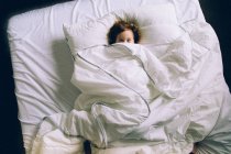 Menina deitada na cama com lençóis brancos — Fotografia de Stock