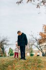 Батько тримає доньку за руку і стоїть під деревом — стокове фото