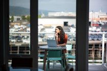 Jovem mulher sentada à mesa e usando laptop e beber café — Fotografia de Stock