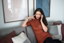 Молодая женщина сидит на диване и разговаривает по телефону — стоковое фото