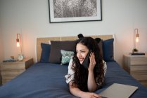 Красива жінка використовує мобільний телефон, лежачи на ліжку вдома — стокове фото