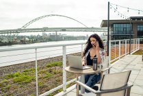 Молода жінка використовує свій мобільний телефон, сидячи на мосту — стокове фото