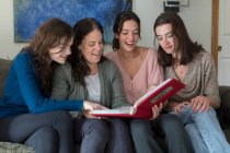 Une mère et ses trois filles rient en regardant un album photo — Photo de stock