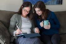 Una madre y su hija trabajan juntas en una tableta - foto de stock