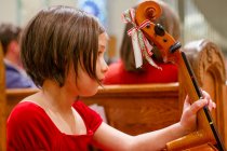Un bambino piccolo con un violoncello siede in un banco della chiesa in attesa di esibirsi — Foto stock
