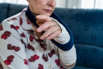 Mulher idosa caucasiana com cabelos brancos com braço quebrado, sofá sentado — Fotografia de Stock