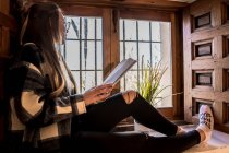 Frau liest Buch bei einer Tasse Tee am Fenster — Stockfoto