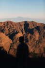 Homem olhando para montanhas rochosas durante o pôr do sol — Fotografia de Stock