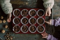 Manos de niño sosteniendo una bandeja de magdalenas de chocolate sin cocer a punto de hornear - foto de stock