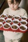 Child holding a tray of unbaked chocolate muffins about to go in oven — Stock Photo