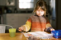 Pequeña pintura de niña preescolar con acuarelas en la mesa de la cocina - foto de stock