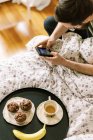 Homme hacing petit déjeuner sur le lit à la maison et en utilisant smartphone — Photo de stock