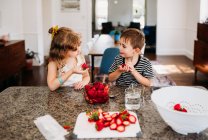 Lindo chico y chica comiendo fresas en casa - foto de stock