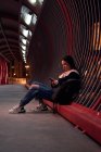 Молода жінка дивиться на свій телефон на червоному мосту вночі — стокове фото