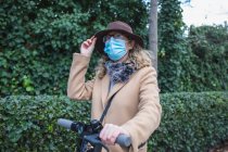 Giovane donna in maschera protettiva e cappello con scooter — Foto stock