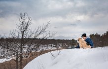 Giovane ragazzo seduto con cane nella neve — Foto stock