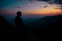 Un hombre mirando al atardecer en la cima de una montaña - foto de stock