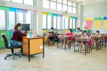 Group of school kids wearing protective mask to Protect Against Covid-19 with teacher sitting in classroom,education,elementary school,Social Distancing,learning and people concept. — Stock Photo