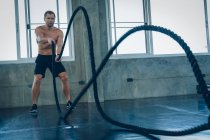 Entrenamiento fuerte del hombre con la cuerda en la aptitud funcional del entrenamiento en el gimnasio, estilo de vida de los músculos del constructor del atleta. - foto de stock