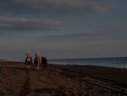 Hommes à cheval sur la plage au coucher du soleil — Photo de stock