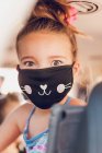 Menina bonita usando uma máscara dentro de um carro. — Fotografia de Stock