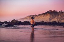Jeune garçon au coucher du soleil sur la plage — Photo de stock