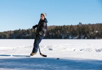 Adolescente jugando hockey en una pista al aire libre en un lago congelado en Canadá. - foto de stock