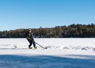 Teenie-Junge spielt Hockey auf einer Eisbahn an einem zugefrorenen See in Kanada. — Stockfoto