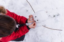 O rapaz com boneco de neve em uma floresta nevada — Fotografia de Stock