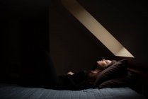 Mulher deitada na cama com os olhos fechados no quarto escuro sob uma luz do céu. — Fotografia de Stock