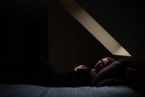 Woman laying on bed with eyes closed in dark room under a sky light. — Stock Photo