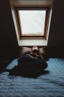 Femme allongée sur le lit dans une pièce sombre regardant à travers une lumière du ciel. — Photo de stock