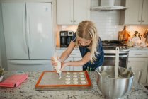 Menina jovem tubulação macarons na cozinha — Fotografia de Stock