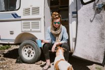 A stylish young woman and her dog sit outside their trailer in the sun — Stock Photo